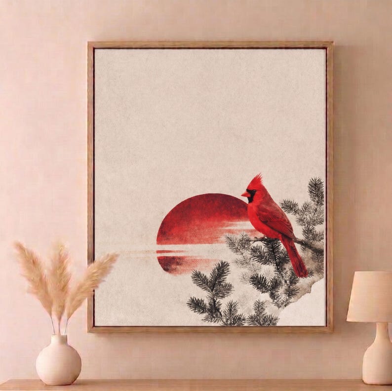 May include: Framed artwork featuring a vibrant red cardinal perched on a branch, set against a backdrop of a red sun and a neutral-toned sky. The artwork has a minimalist style with a wooden frame.