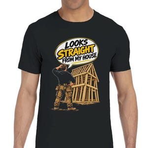May include: A black short-sleeve t-shirt featuring a graphic of a person in work clothes standing before a wooden house frame. Above the figure is a speech bubble with the text "LOOKS STRAIGHT FROM MY HOUSE" in yellow and black lettering.