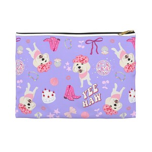 May include: A lavender zippered pouch with a repeating pattern of cartoon dogs wearing cowboy hats and bandanas, pink cowboy boots, disco balls, and the text "Yee Haw". Other elements include bows, cherries, and seashells.