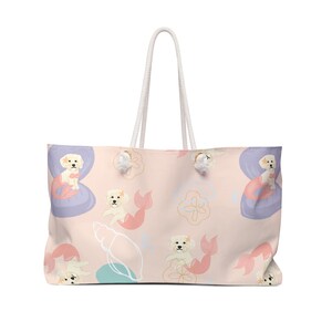 May include: A large tote bag with a light pink background featuring a repeating pattern of cartoon dogs with mermaid tails, seashells, and floral accents. The bag has white rope handles.