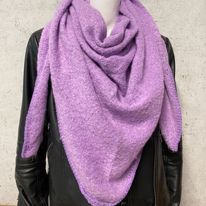 May include: A soft, purple scarf with a fuzzy texture and a contrasting light purple trim. The scarf is folded and draped over a mannequin wearing a black leather jacket.