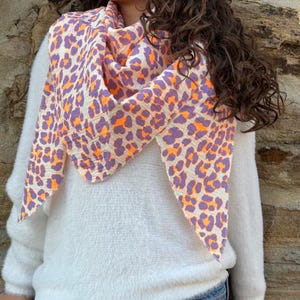 May include: A white fluffy sweater with a purple and orange leopard print scarf. The scarf is tied around the neck and hangs down the front of the sweater.