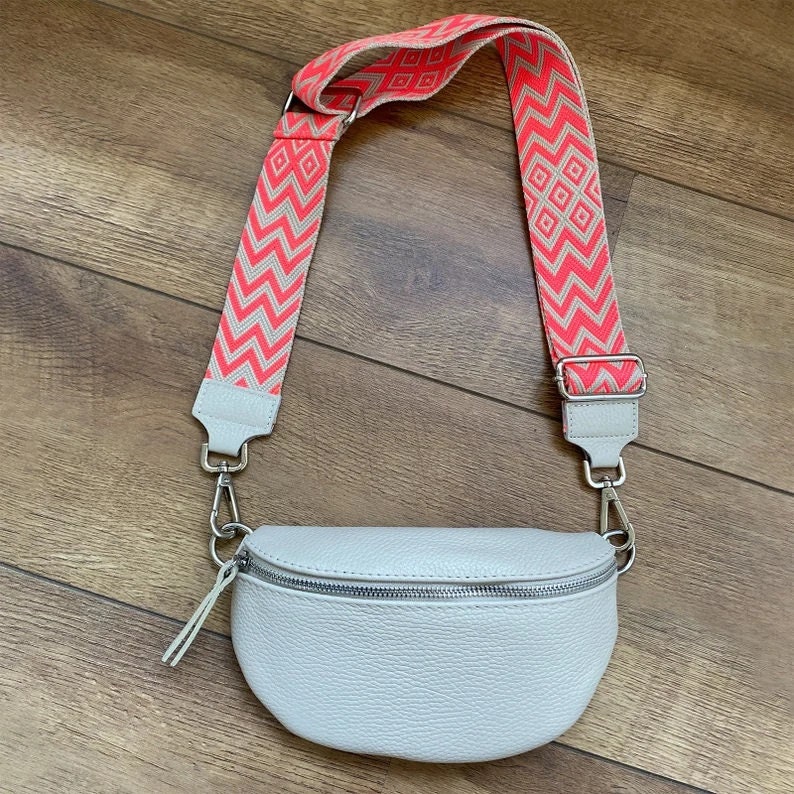May include: A light gray leather fanny pack with a zipper closure and a pink and white patterned adjustable strap.