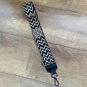 May include: Black and white patterned fabric strap with a silver hook and a black leather loop.