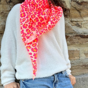 May include: A pink and orange leopard print scarf worn with a white fluffy sweater and blue jeans.