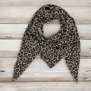 May include: A triangular scarf with a leopard print pattern in shades of brown and black on a light wood background.