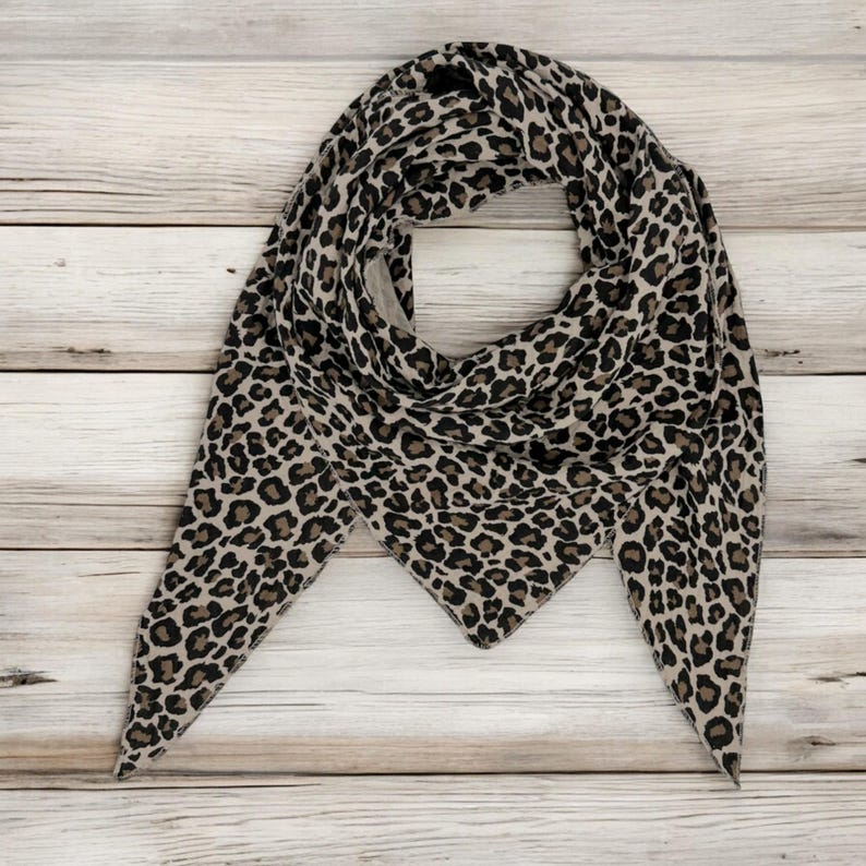 May include: A triangular scarf with a leopard print pattern in shades of brown and black on a light wood background.