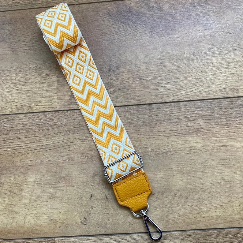 May include: A yellow and white patterned fabric strap with a yellow leather adjustable buckle and a silver hook.