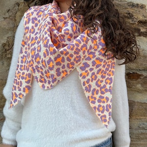 May include: A white fluffy sweater with a purple and orange leopard print scarf. The scarf is tied around the neck and hangs down the front of the sweater.