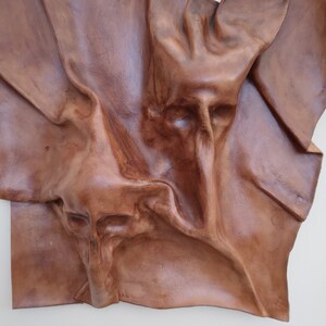 Könnte beinhalten: Eine braune Lederwandskulptur mit einem strukturierten, abstrakten Design. Das Leder ist gefaltet und drapiert, um einen dreidimensionalen Effekt zu erzeugen.