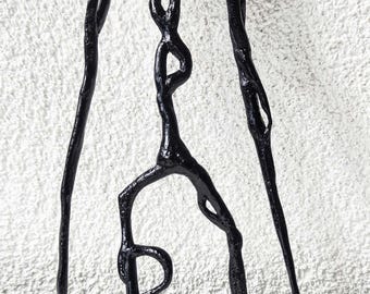 May include: A black, glossy, three-dimensional sculpture of a tall, slender, humanoid figure with elongated limbs, a rounded head, and thin, pointed hands. The figure has a textured, organic appearance with a central vertical structure.