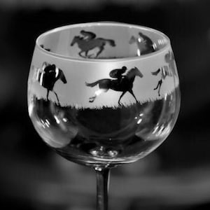 Op de afbeelding: Een helder glazen kelk met een ronde kom en een lange steel. De kelk is gegraveerd met een ontwerp van rennende paarden.