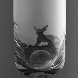 May include: A tall, clear glass vase with a frosted upper section and a decorative, dark silhouette design near the base. The vase has a slender, cylindrical shape and a wide opening. The design appears to be a deer.