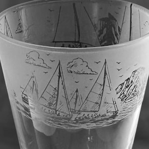 May include: A clear glass tumbler with a nautical design. The upper portion of the glass features a frosted band with etched sailboats, clouds, and birds. The glass has a slightly flared shape and a smooth, transparent finish.