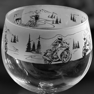 May include: A clear glass with a black and white design of a motorcycle rider on a winding road. The glass is a stemmed goblet style.