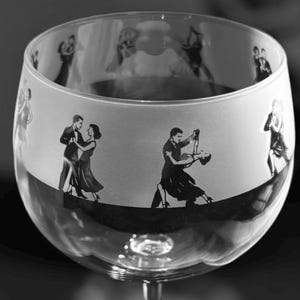 Könnte beinhalten: Ein klares Glas mit einem mattierten Design von tanzenden Paaren. Das Glas hat eine breite Schale und einen langen Stiel.