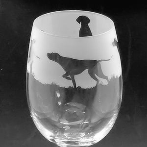 Puede incluir: Una copa de vino de vidrio transparente con un diseño grabado de dos siluetas negras de perros apuntando. La copa tiene un tallo largo y una base redonda.