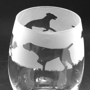 Pode incluir: Uma taça de vinho de vidro transparente com um design fosco que apresenta silhuetas de cães. Os cães estão em várias poses, incluindo correr e ficar de pé. A taça tem um fundo arredondado e uma borda larga.