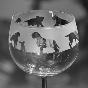 May include: A clear glass wine glass with a frosted design of various dog silhouettes. The glass has a round bowl and a long stem.