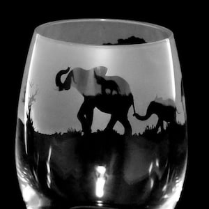 以下が含まれることがあります： 2頭の象が並んで歩いているエッチングデザインが施された透明なガラス製のワイングラスです。1頭は他方よりも大きいです。