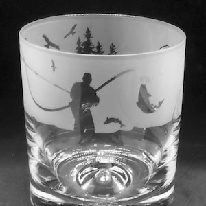 May include: A frosted glass tumbler with a silhouette of a person fishing with a rod and reel. The design also includes trees and birds.
