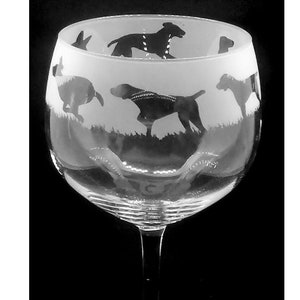 Puede incluir: Una copa de vino de vidrio transparente con un diseño esmerilado de un grupo de perros corriendo por la hierba alta. Los perros están en silueta negra.
