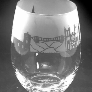 May include: A clear glass wine glass with a frosted design of a bridge and buildings. The design is in black and white.