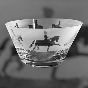 Könnte beinhalten: Eine klare Glasschale mit ausgestellter Form, die geätzte Silhouetten von Reitern auf Pferden zeigt. Das Design der Schale umfasst eine grasbewachsene Basis und eine Reihe von Reitern in verschiedenen Posen, die ein Vintage-Reitmotiv schaffen.
