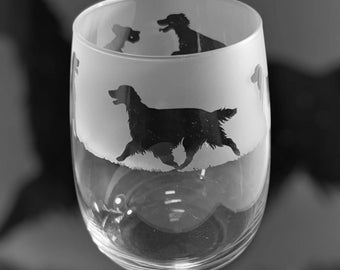 May include: A clear stemless wine glass with a frosted band featuring black silhouettes of dogs in various poses. The glass has a rounded shape and is designed for wine.