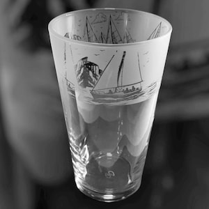 May include: A clear glass with a nautical design. The glass features etched images of sailboats, clouds, and a rocky island. The design is in black and white, creating a classic and elegant look. The glass is tall and cylindrical.