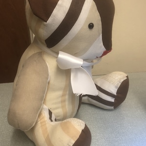 May include: A brown and cream striped plush teddy bear with a white satin bow. The bear has black button eyes and a red stitched nose.