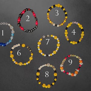May include: Nine beaded bracelets in various designs are displayed against a dark background. The bracelets feature a variety of beads in colours like yellow, black, red, white, and blue. Some bracelets have letter beads spelling out words.