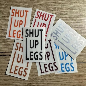 Könnte beinhalten: Ein Set mit sechs Aufklebern mit dem Spruch "Shut Up Legs" in verschiedenen Farben, darunter Schwarz, Rot, Orange, Blau und Silber.