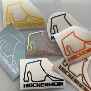Könnte beinhalten: Ein Set mit acht Aufklebern, die den Hockenheimring-Rennkurs in verschiedenen Farben zeigen, darunter Gelb, Orange, Schwarz, Blau und Irisierend. Jeder Aufkleber trägt den Namen "Hockenheim".