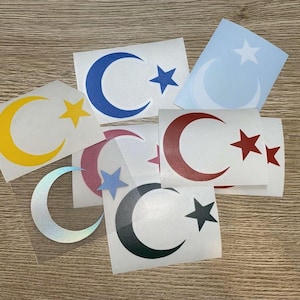 Könnte beinhalten: Sortiment an Halbmond- und Stern-Aufklebern in verschiedenen Farben, darunter Gelb, Blau, Rot, Schwarz und Weiß. Die Aufkleber befinden sich auf weißem Papier.