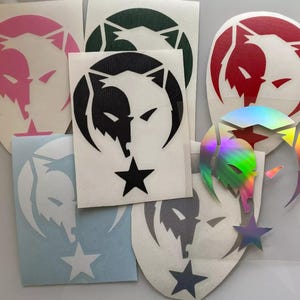 Könnte beinhalten: Ein Set mit zehn Vinyl-Aufklebern mit einem Wolfskopf-Design und einem Stern. Die Aufkleber sind in verschiedenen Farben, darunter rosa, rot, schwarz, grün und schillernd.