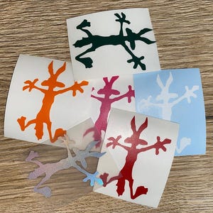 Könnte beinhalten: Fünf verschiedene Vinyl-Aufkleber mit einem Cartoon-Coyote-Design. Die Aufkleber sind in verschiedenen Farben, darunter Orange, Rot, Grün, Blau und schillernd.