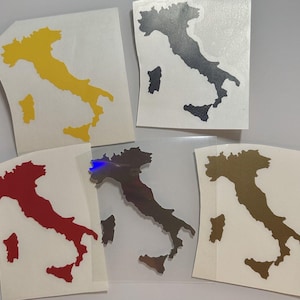 Puede incluir: Una colección de pegatinas de vinilo con la forma de Italia. Las pegatinas son de varios colores, incluyendo amarillo, negro, rojo, iridiscente y dorado. Cada pegatina está sobre un respaldo blanco, con la península italiana y las islas claramente definidas.