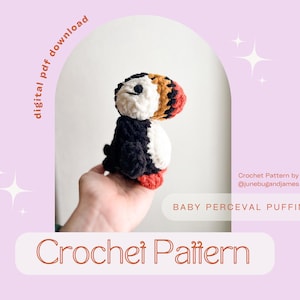 May include: Crochet pattern for a baby puffin amigurumi toy. The puffin is white, black, and orange with a black beak and small black eyes. The pattern is by @junebugandjames and is called "Baby Perceval Puffin".