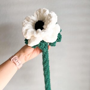 May include: A white crocheted flower with a black center and a green crocheted stem.