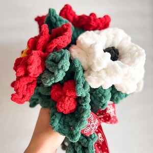May include: A crocheted bouquet of red poinsettia flowers, white flowers, and green leaves tied with a red ribbon with white snowflakes.