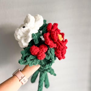 May include: A bouquet of crocheted flowers in white, red, and green. The flowers are made with yarn and have a fluffy texture.