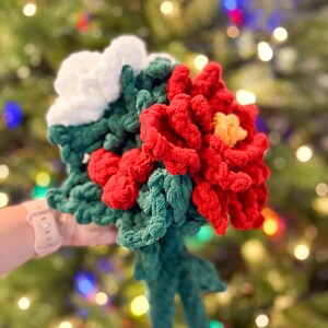 May include: A crocheted bouquet of red poinsettias with white flowers and green leaves.