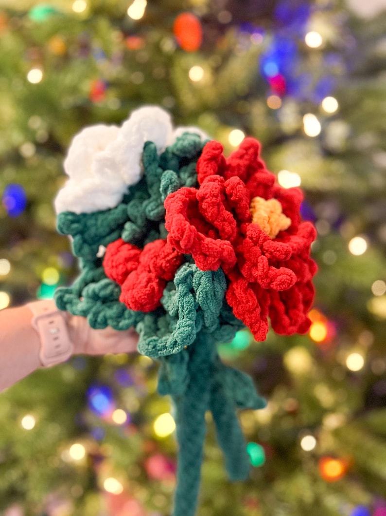 May include: A crocheted bouquet of red poinsettias with white flowers and green leaves.