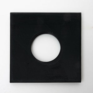 Könnte beinhalten: Ein schwarzes quadratisches Plastikteil mit einem runden Loch in der Mitte.