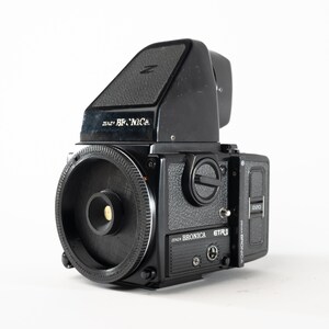 Puede incluir: Una cámara Bronica ETR negra con una lente negra y un visor negro. La cámara tiene una etiqueta plateada que dice "Bronica ETR" y una etiqueta plateada que dice "2000" en el lateral.