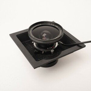 May include: A black and silver camera lens with a black metal frame and a silver lens cap. The lens is mounted on a black metal base with a black metal lever.