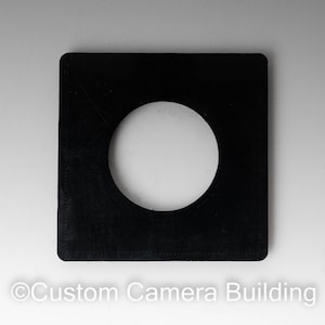 May include: A black square-shaped camera film holder with a round hole in the center.