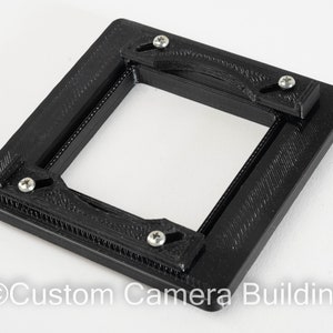 Op de afbeelding: Zwarte 3D-geprinte camera filmrug met vier schroeven. De filmrug heeft een vierkante opening voor een filmnegatief.