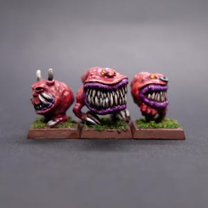 May include: Three red and purple painted miniature figures with sharp teeth and horns. The figures are standing on small brown bases.